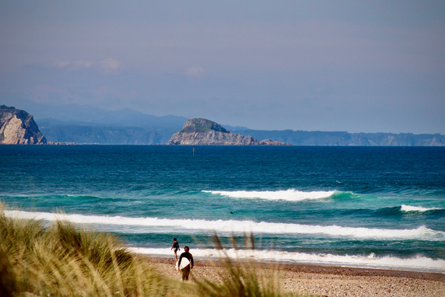 Surfistas en Xagó con la isla de La Deva al fondo