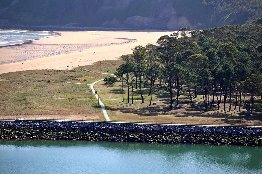 Vista del paseo de la ría de Villaviciosa con la playa de Rodiles al fondo y la arboleda en primer término