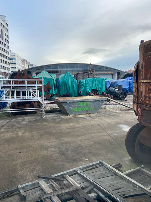Elementos ferroviarios para rehabilitación estacionados y cubiertos con lonas en la zona de reserva no accesible al público en el museo del ferrocarril en Gijón