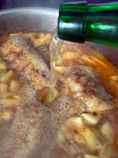 Añadiendo la sidra al guiso de merluza a la sidra